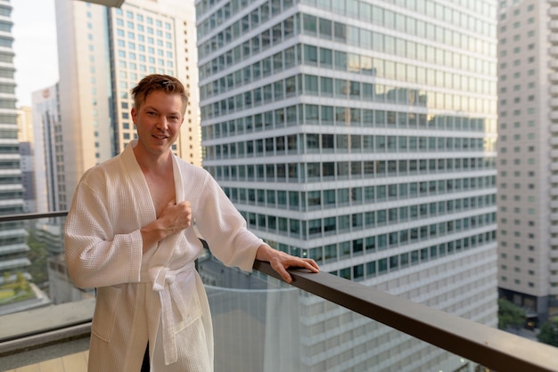 Portret van de jonge knappe man die vanaf het balkon geniet van het uitzicht over de stad