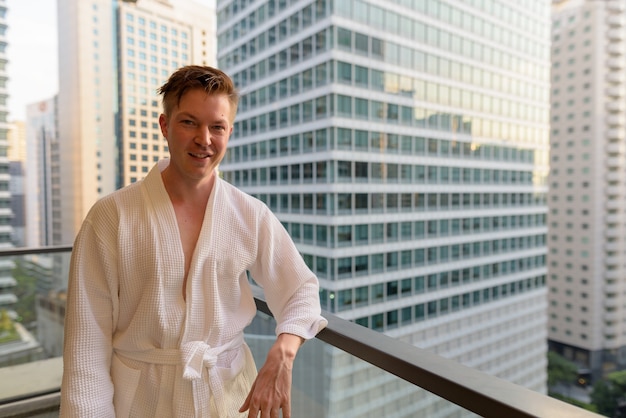 Portret van de jonge knappe man die vanaf het balkon geniet van het uitzicht over de stad