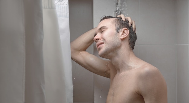 Portret van de jonge knappe man wast zichzelf met douchegel, schuimt hoofd met shampoo in de badkamer thuis close-up