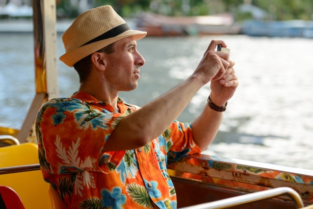 Portret van de jonge knappe toeristenman die boot berijdt als openbaar vervoer in de stad van bangkok