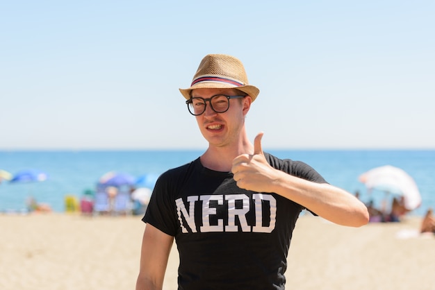 Portret van de jonge knappe toeristenmens als nerd op het strand in Spanje