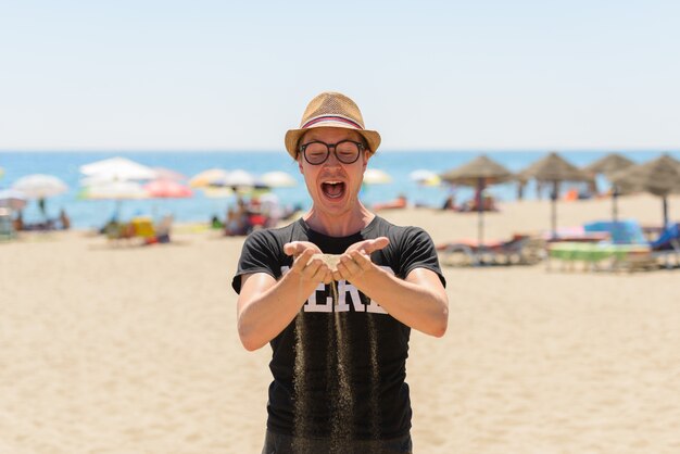 Portret van de jonge knappe toeristenmens als nerd op het strand in Spanje