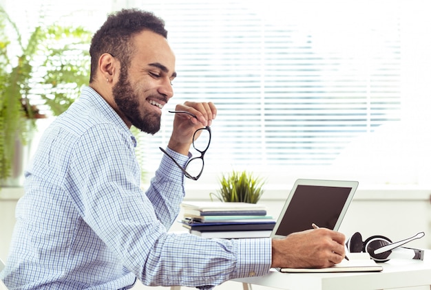 Portret van de knappe Afrikaanse zwarte jonge bedrijfsmens die aan laptop op kantoor werkt