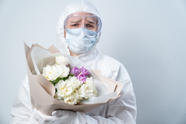 Portret van de vrouw van de dokter in beschermend pak, masker, bril en handschoenen met boeket bloemen.