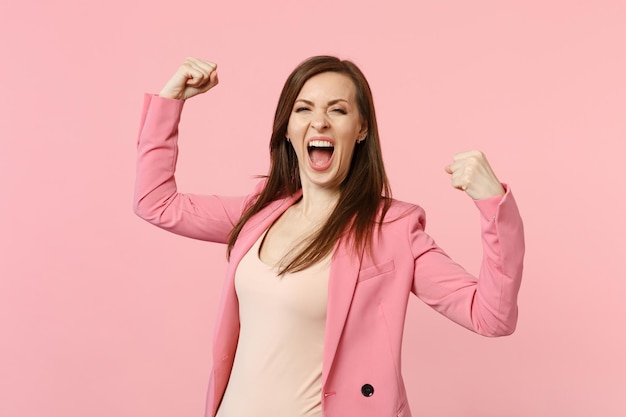 Portret van dolblij schreeuwende jonge vrouw in jas balde vuisten als winnaar geïsoleerd op pastel roze muur achtergrond in studio. Mensen oprechte emoties, lifestyle concept. Bespotten kopie ruimte.