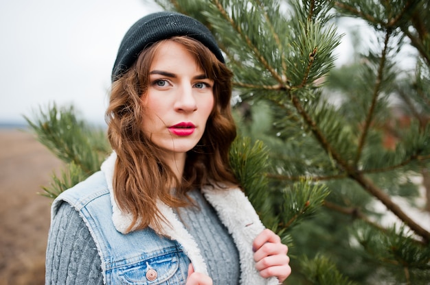 Portret van donkerbruin meisje in hoed en jeansjasje bij boom.