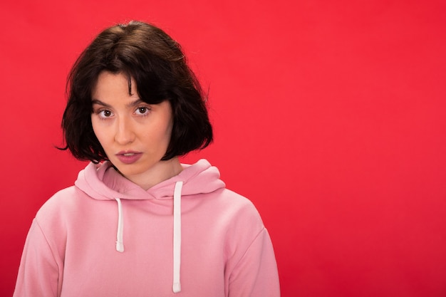 Portret van doordachte brunette meisje in roze hoodie voorzijde kijken close-up