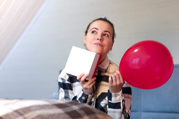 Portret van doordachte peinzende meisjesholding in handen huidige doos en rode ballon