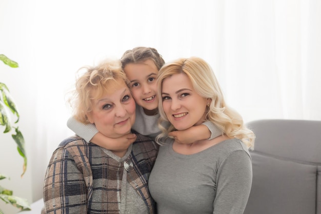 Portret van drie generaties vrouwen kijken naar camera poseren voor familiefoto, schattig klein meisje knuffel moeder en oma genieten van tijd thuis, glimlachende moeder, dochter en grootmoeder brengen weekend samen door