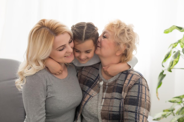 Portret van drie generaties vrouwen kijken naar camera poseren voor familiefoto, schattig klein meisje knuffel moeder en oma genieten van tijd thuis, glimlachende moeder, dochter en grootmoeder brengen weekend samen door