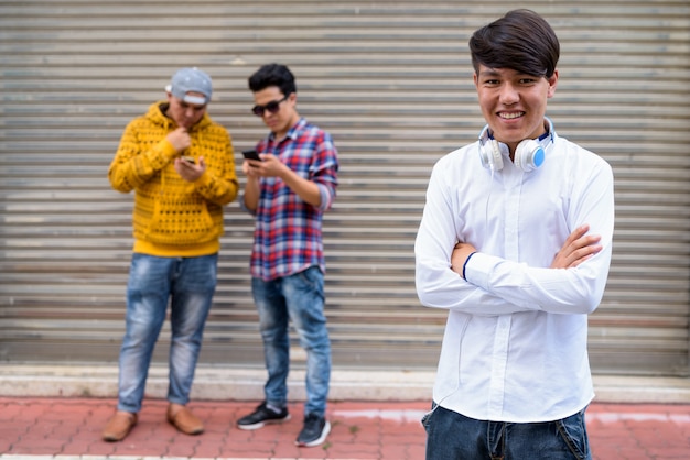 Portret van drie jonge Aziatische mannen permanent tegen magazijn deur in de straten van Bangkok, Thailand