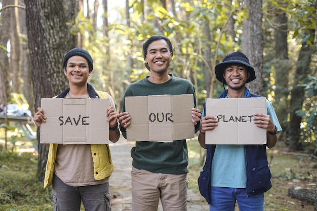 Portret van drie jonge mannelijke eco-activisten die in een groen zonnig park staan en een bord vasthouden met de woorden S