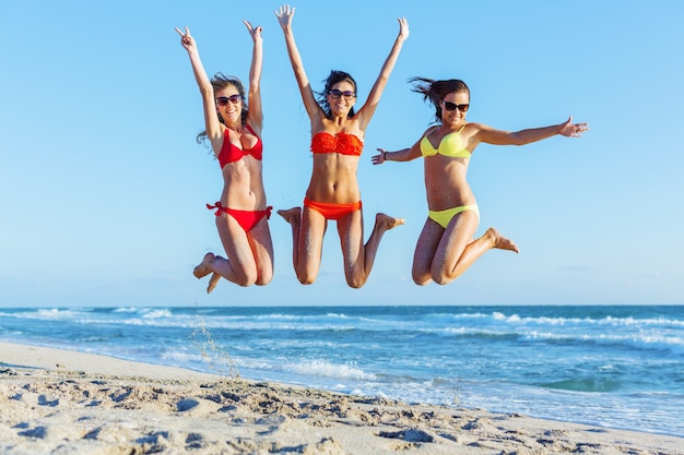 Portret van drie jonge vrouwenvrienden die op de kust springen