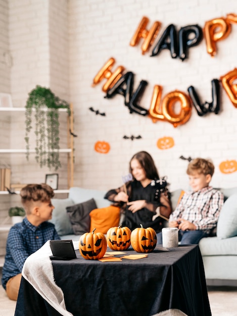 Portret van drie kinderen die aan het chatten zijn tijdens Halloween-feest terwijl ze aan tafel in een ingerichte kamer staan