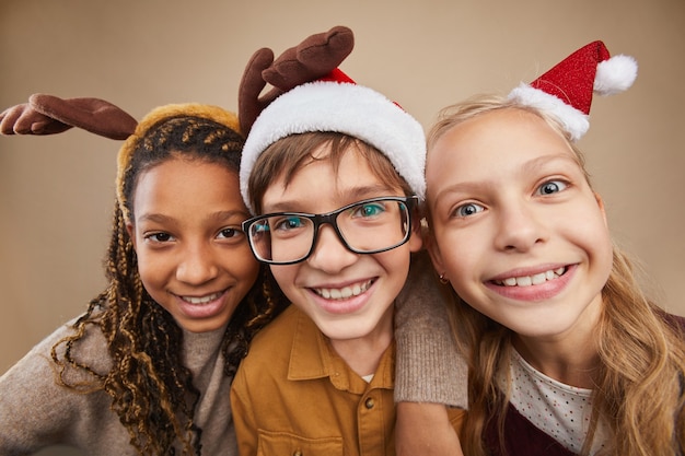 Portret van drie kinderen die kerstportretten dragen en glimlachen naar de camera terwijl ze tegen de achtergrond in de studio staan