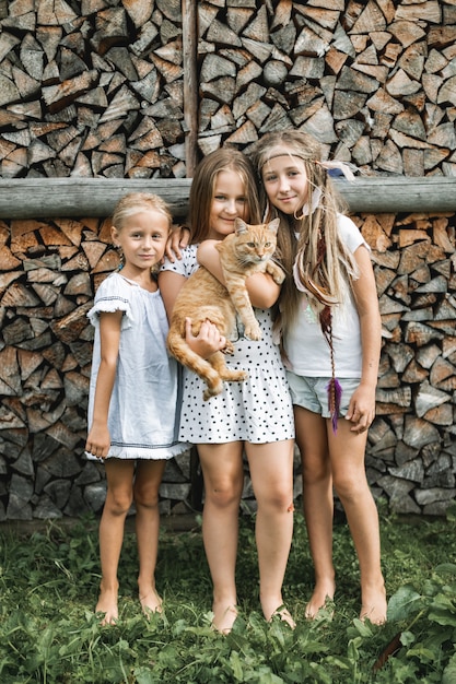 Portret van drie kleine mooie meisjes, zusters, in vrijetijdskleding, permanent samen op de achtergrond van gestapeld brandhout