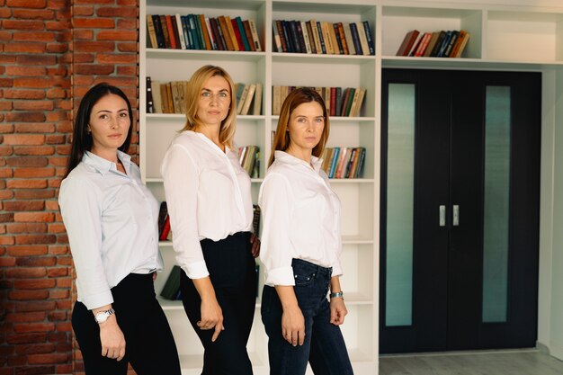 Portret van drie succesvolle zakelijke vrouwelijke medewerkers in witte overhemden glimlachen, terwijl ze in kantoor. Mensen, zaken en teamwork concept. Horizontaal schot. Vooraanzicht.