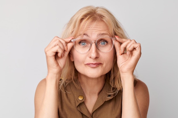 Portret van een 50-jarige dame loensend in een bril geïsoleerd op een witte studio achtergrond Visiecontrole en verlies van gezichtsvermogen zoekconcept brillenwinkel