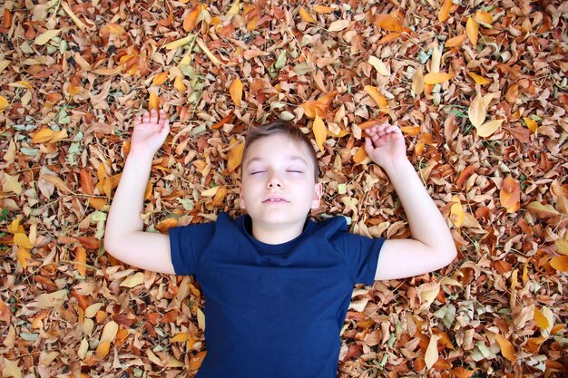 Portret van een 9-jarige jongen in een herfstpark in een blauw T-shirt ligt in oranje gevallen bladeren