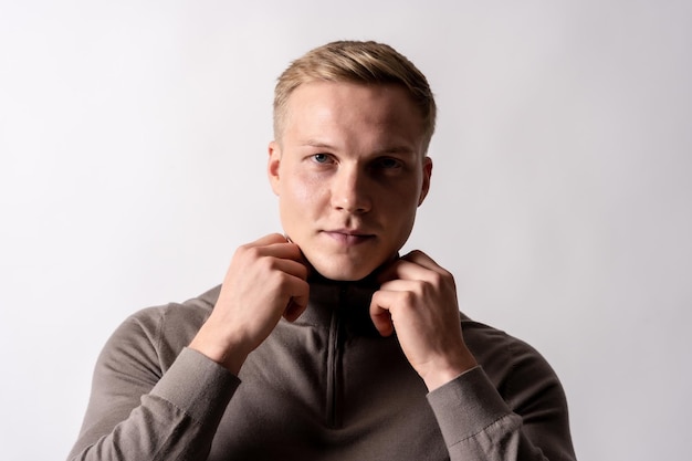 Portret van een aantrekkelijk blond Duits model met een bruine trui op een witte achtergrond kijkend naar de camera