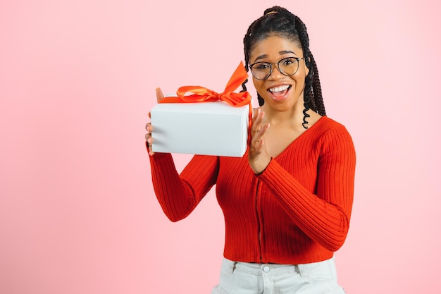 Portret van een aantrekkelijk creatief minded vrolijk meisje dat in handen een cadeau-kopieerruimte vasthoudt, geïsoleerd over een roze pastelkleurige achtergrond