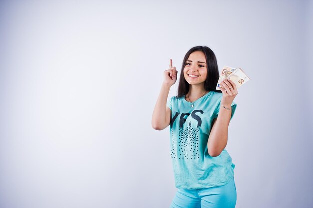 Portret van een aantrekkelijk meisje in blauwe of turquoise t-shirt en broek poseren met veel geld in haar hand