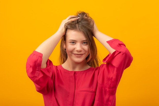 Portret van een aantrekkelijk meisje met de handen achter het hoofd glimlacht en kijkt in de camera Jonge vrouw op gele achtergrond