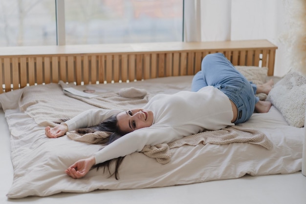 Portret van een aantrekkelijk vrolijk meisje in het wit dat in bed ligt met een ontspannende pose en een goed humeur