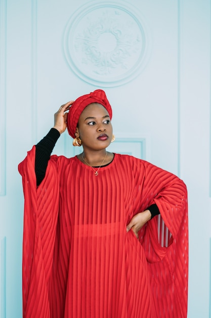 Portret van een aantrekkelijke Afrikaanse vrouw die wegkijkt op de blauwe muurachtergrond. Vrouw in rode kleren en hoofddoek poseren in studio.