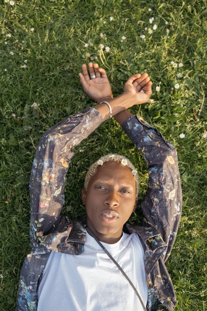 Foto portret van een aantrekkelijke afro-amerikaanse man met stijlvol haar die naar een camera kijkt die op gras ligt