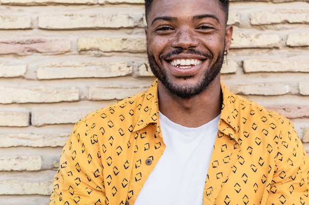 Portret van een aantrekkelijke Amerikaanse man met baard en een piercing gele shirt dragen in een bakstenen muur