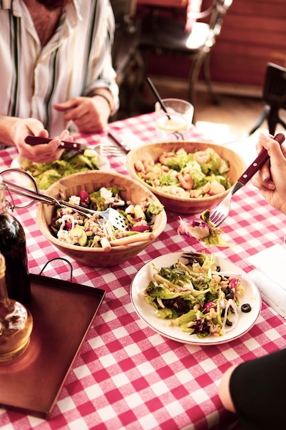 Foto portret van een aantrekkelijke blanke lachende vrouw die salade eet, focus op hand en vork