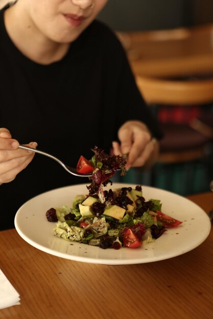 Portret van een aantrekkelijke blanke lachende vrouw die salade eet, focus op hand en vork