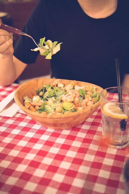 Portret van een aantrekkelijke blanke lachende vrouw die salade eet, focus op hand en vork