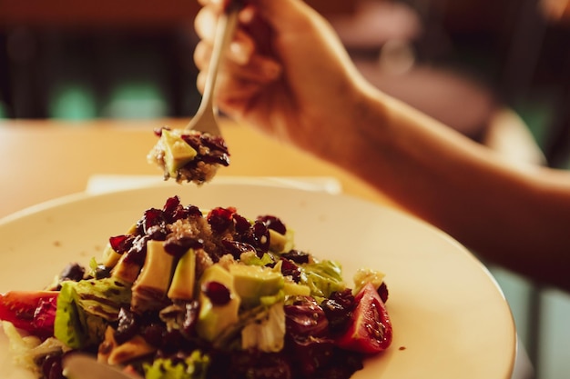 Portret van een aantrekkelijke blanke lachende vrouw die salade eet, focus op hand en vork