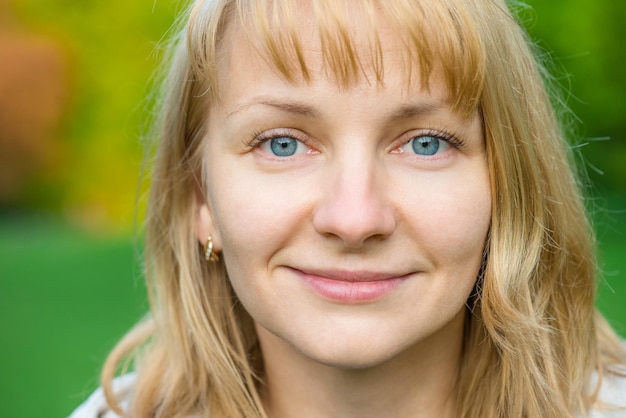 Portret van een aantrekkelijke glimlachende blanke jonge vrouw in het lentepark die dicht bij de camera kijkt