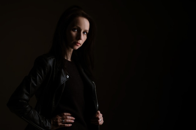 Portret van een aantrekkelijke jonge donkerbruine vrouw in een zwart leerjasje die zich op een zwarte achtergrond bevindt