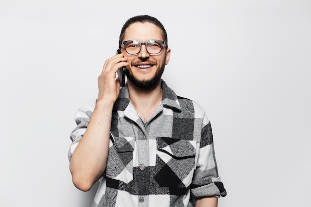 Portret van een aantrekkelijke jonge glimlachende man in een geruit hemd die op een smartphone praat