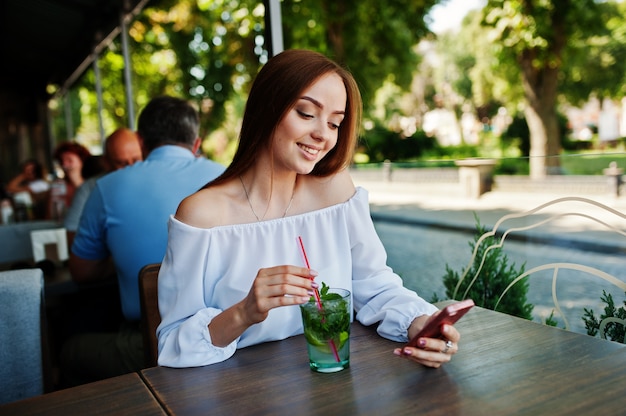 Portret van een aantrekkelijke jonge onderneemster met een mojitococktail die een bericht op haar smatphone texting.