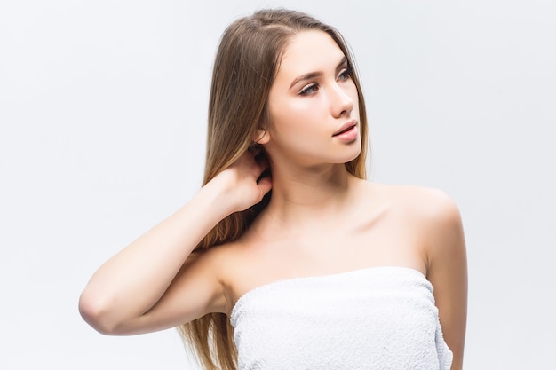 Portret van een aantrekkelijke jonge vrouw die de gladde en gezonde huid van haar gezicht aanraakt en wegkijkt tegen de witte muur