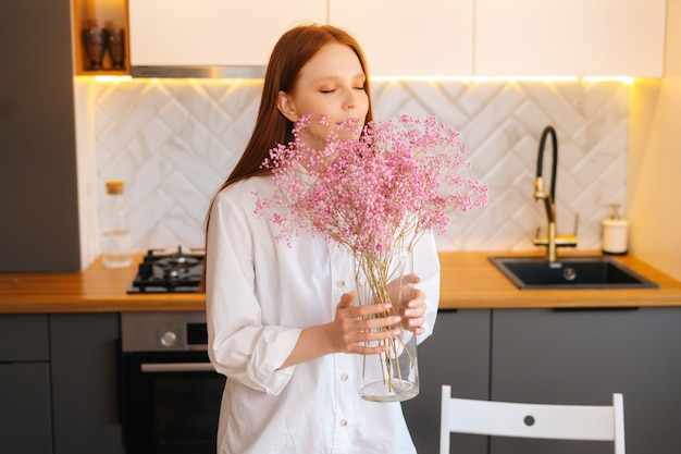 Portret van een aantrekkelijke jonge vrouw die een aromatisch gypsophila-bloemenboeket ruikt in een gezellige woonkamer