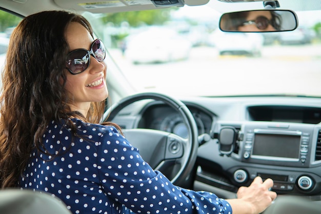 Portret van een aantrekkelijke jonge vrouw in een vrijetijdskleding die over haar schouder kijkt terwijl ze achter het stuur zit en een auto bestuurt