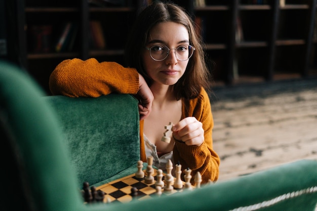 Portret van een aantrekkelijke jonge vrouw met een elegante bril die een schaakbeweging maakt met een ridderstuk dat in de vloer zit en naar de camera kijkt