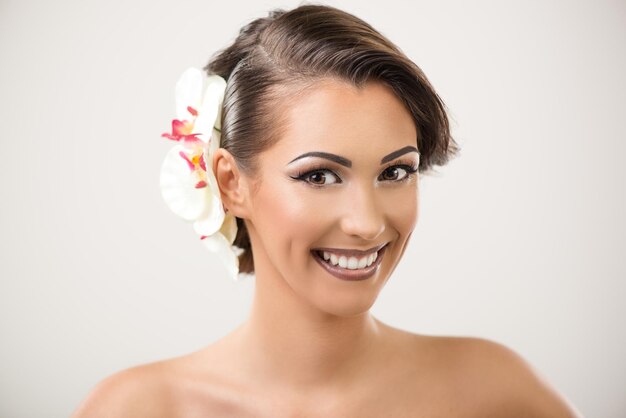 Portret van een aantrekkelijke jonge vrouw met mooie make-up en witte orchidee in haar haar poseren in een studio. Camera kijken.