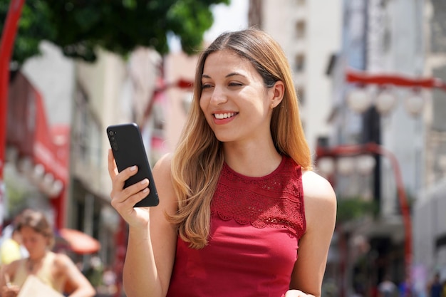 Portret van een aantrekkelijke lachende vrouw die in Sao Paulo City loopt en sms't op mobiele telefoon met onscherpe achtergrond