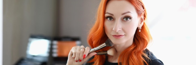 Portret van een aantrekkelijke make-upartiest die penselen vasthoudt voor luxe werkstudio's voor verschillende