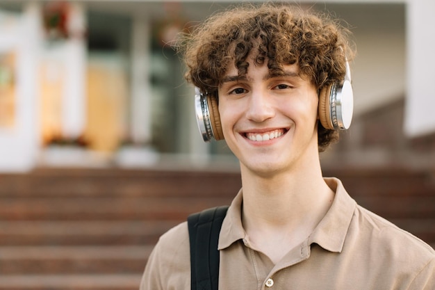 Portret van een aantrekkelijke mannelijke student met krullend haar in een koptelefoon die lacht