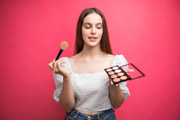 portret van een aantrekkelijke, mooie jonge vrouw die geïsoleerd staat over een roze achtergrond en make-up vasthoudt