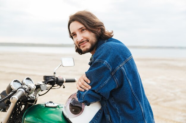 Portret van een aantrekkelijke positieve blije gelukkige man fietser op zijn fiets buiten op een strand.