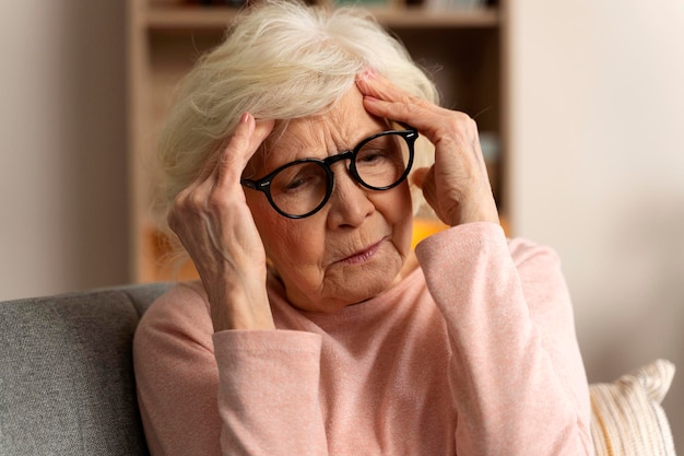 Portret van een aantrekkelijke senior vrouw die thuis op de bank zit met hoofdpijn die pijn voelt en met uitdrukking van onwel zijn Gezondheidsproblemen concept